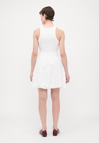 Weißes ärmelloses Kleid mit einem figurbetonten Oberteil und einem schwingenden Rock. Aus weichem Stoff gefertigt, verfügt es über eine geraffte Taille und eine glatte Oberfläche.