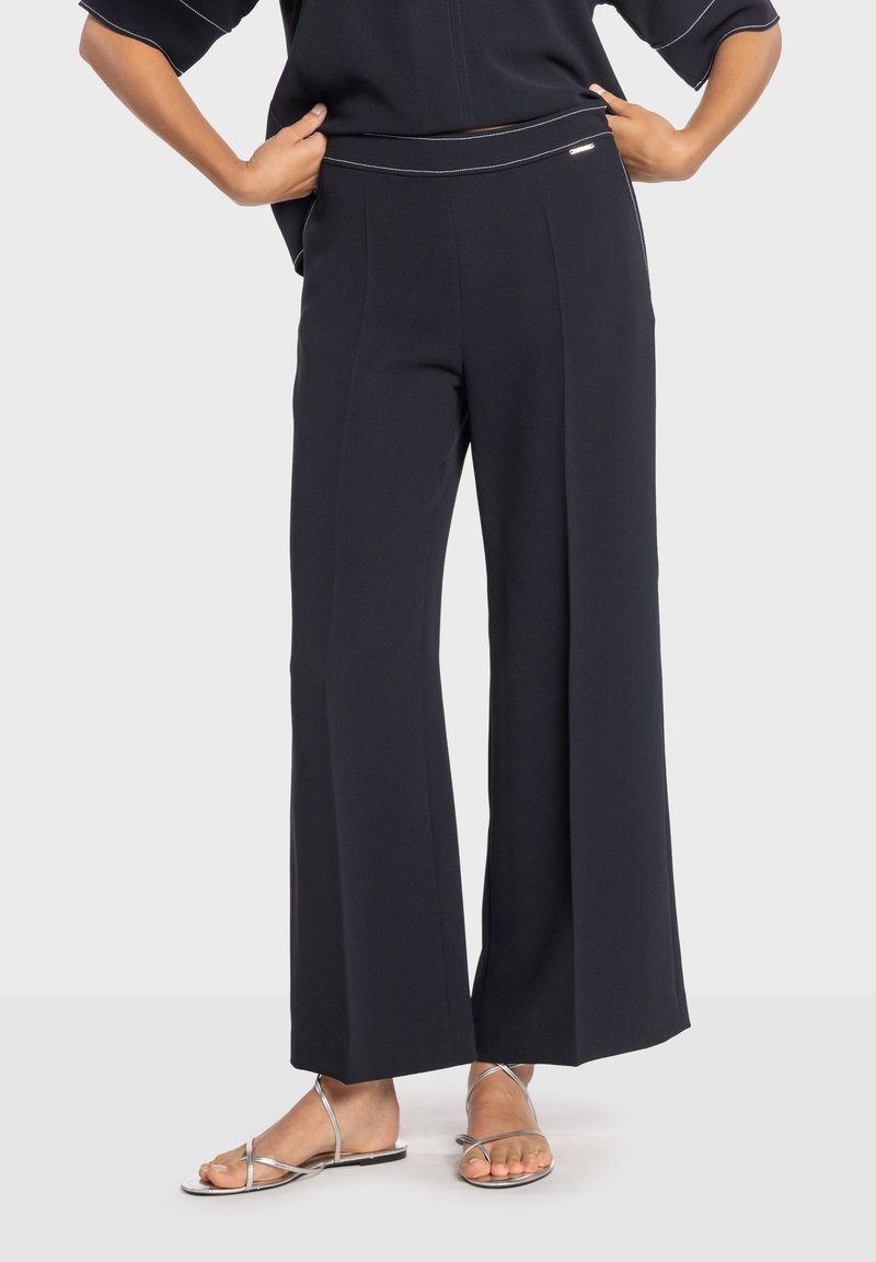 Pantalones de pierna ancha color azul marino con textura suave, que presentan pinzas delanteras y costuras en contraste. Completados con un acento de herrajes brillantes en la cintura.