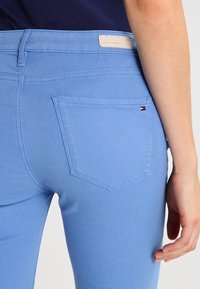 Jeans de mezclilla azul con un diseño ajustado, que cuentan con un bolsillo trasero y una pequeña etiqueta de logo. La tela tiene una textura suave.