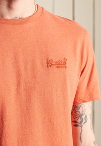 Kortærmet orange t-shirt lavet af struktureret stof, med et lille broderet logo på brystet. Rund halsudskæring og almindelig pasform.