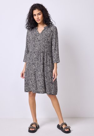 Vestido de flores en blanco y negro con mangas tres cuartos, escote en V y un dobladillo acampanado, combinado con sandalias negras gruesas.