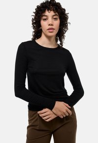 Haut noir à manches longues en tissu léger. Présente un col rond et des manches ajustées. Associé à un pantalon marron.