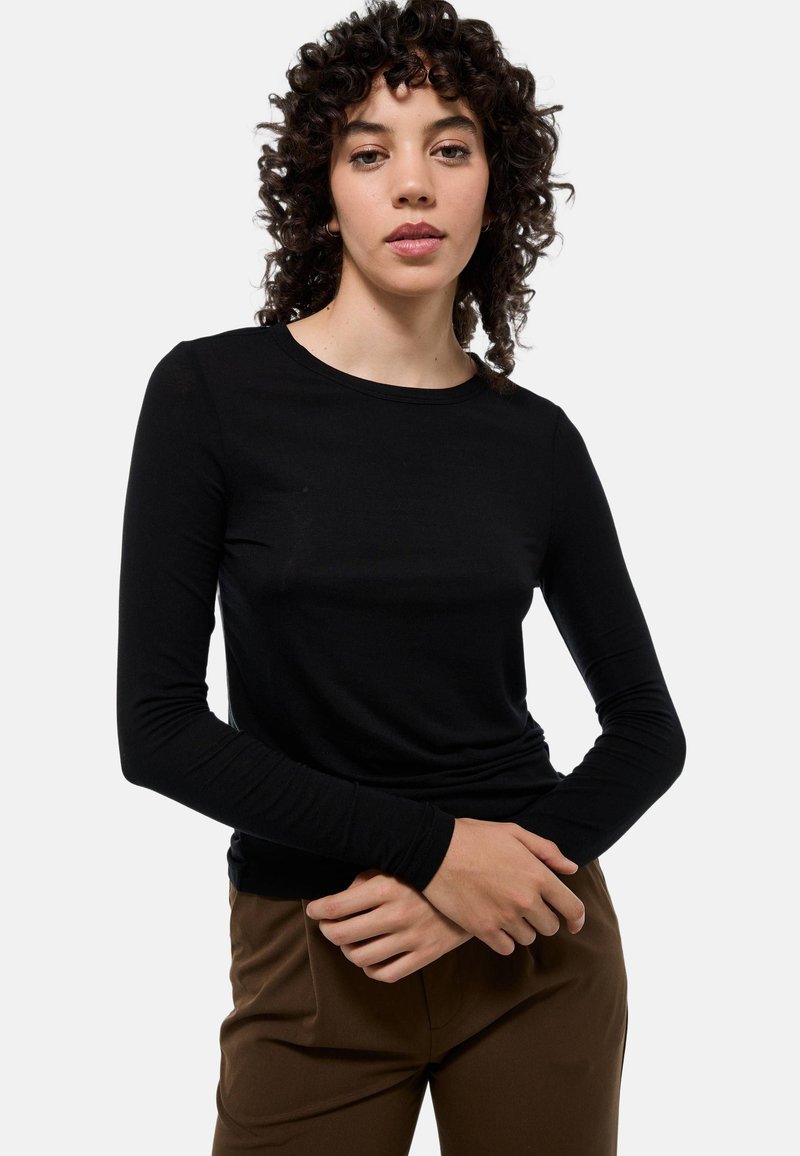 Haut noir à manches longues en tissu léger. Présente un col rond et des manches ajustées. Associé à un pantalon marron.