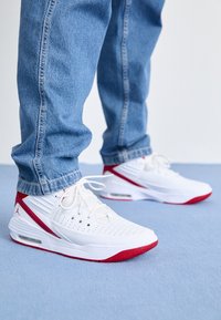 Scarpe da ginnastica bianche con accenti rossi, caratterizzate da una suola testurizzata, parte superiore perforata e chiusura con lacci. Abbinate a jeans blu.