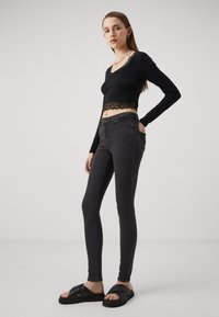 Svart langermet crop topp med blonder, kombinert med trange mørkegrå jeans og svarte tversover-sandaler. Enkel, stilren design.