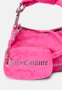 Rozā samtaina rokassoma ar noņemamu minisomu, sudraba aksesuāriem un reljefa "Juicy Couture" logotipu priekšpusē. Gluda tekstūra.