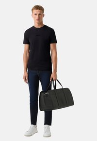 Černé tričko s logem, tmavé džíny, bílé tenisky a velká černá kožená taška přes rameno s pevnými popruhy a elegantním designem.