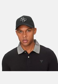 Polo negro con cuello gris y detalles de logo; cuenta con una tapeta de botones. Gorra negra con logo bordado gris en la parte delantera.