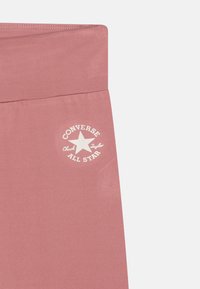 Rosa elastisk stoff med en glatt overflate som viser en hvit trykt logo av "Converse Chuck Taylor All Star" og en stjernegrafikk.