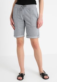 Szare bawełniane szorty z elastycznym paskiem w talii i sznurkiem do ściągania, z dwoma przednimi kieszeniami i wywiniętymi mankietami. Połączone z czarnymi płaskimi sandałami.