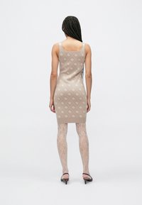 Bēša adīta kleita ar ģeometriskām rakstām un piegulošu siluetu. Kopā ar caurspīdīgām mežģīņu zeķbikēm un papēžu apaviem, demonstrējot nevainojamu dizainu.