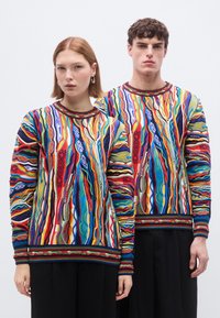 Pulls en tricot présentant des motifs multicolores vibrants avec des designs ondulés. Encolures côtelées et bordures noires contrastantes en bas.