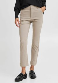 Beige slim-fit kalhoty s dobře padnoucím střihem, hladkým předním dílem a kotníkovým lemem, v kombinaci s černými mokasínami. Hladká tkanina z bavlněného směsového materiálu.