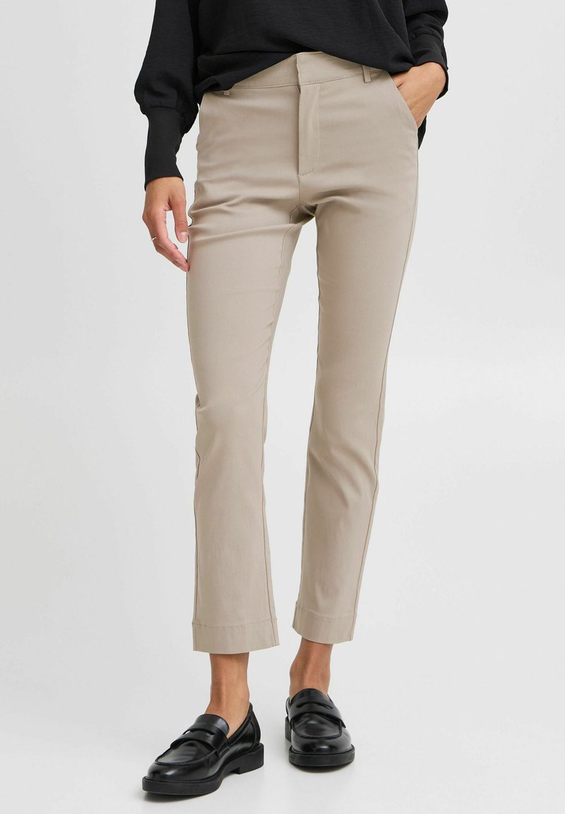 Beige slim-fit kalhoty s dobře padnoucím střihem, hladkým předním dílem a kotníkovým lemem, v kombinaci s černými mokasínami. Hladká tkanina z bavlněného směsového materiálu.
