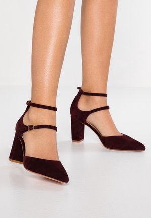 Chaussures à talons hauts en daim bordeaux avec un bout pointu et des brides à la cheville. Elles présentent un talon carré et des côtés ouverts pour un design moderne.