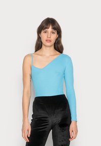 Bodysuit canelado azul claro com uma manga curta e uma longa, combinado com calças de veludo pretas de cintura alta.