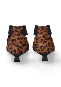 Een paar kitten heel schoenen met een luipaardprint en zwarte elastische enkelbandjes, gezien vanaf de achterkant tegen een witte achtergrond.