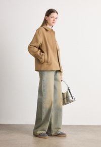 Tan uldblandede jakke med sidelommer, parret med løstsiddende falske blå jeans. Sølv håndtaske med kontrastbranding, grå slip-on sko.