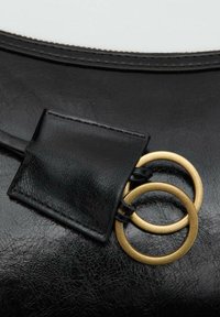 Sort læder håndtaske detalje; tekstureret overflade, guld hardware med to ringe og et rektangulært lædermærke hæftet på.