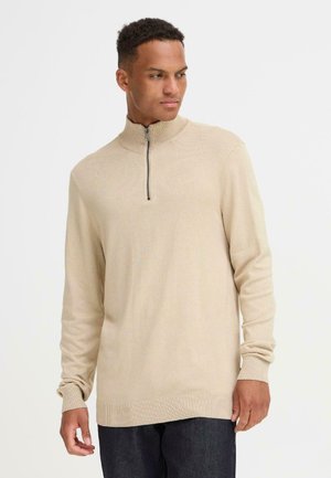 Beige zip-neck genser laget av et mykt strikket stoff. Den har lange ermer og ribbestrikkede mansjetter, med en jevn tekstur og en avslappet passform.