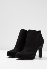 Bottines en suede noir à bout arrondi, talon haut et texture lisse. Design simple sans matériel ou embellissements visibles.