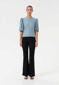 Light blue, short-sleeve top with puffed sleeves, paired with black flared pants. Smooth fabric, simple round neckline, minimal detailing.