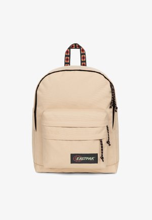 Mochila beige con un acabado textil suave, que cuenta con un bolsillo frontal, correas ajustables y un asa superior con patrón y acentos rojos.