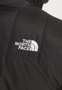 Gros plan sur l'épaule d'une veste noire avec le logo The North Face brodé en blanc sur le tissu.
