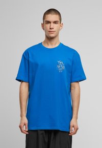 Kortærmet blå bomulds t-shirt med et grafisk print i hvidt på venstre brystområde. Løs pasform og rund halsdesign.