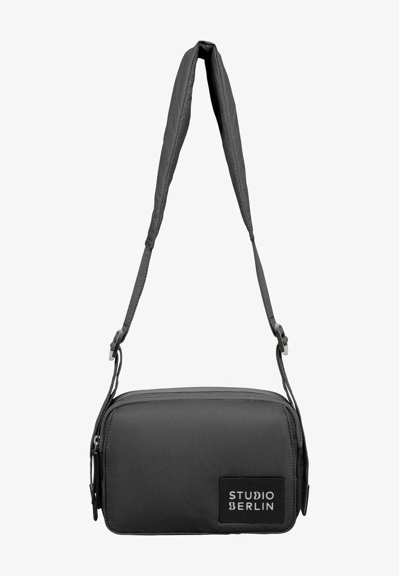 Harmaa olkalaukku, joka on valmistettu sileästä kankaasta, suorakulmainen muoto, vetoketjusulku ja säädettävä olkahihna; edessä on logopatchi.