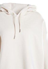 Pulóverová mikina s kapucňou v svetlobéžovej látke s jemnou textúrou, s kapucňou na sťahovanie a kovovými koncovkami na šnúrkach.