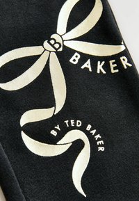 Tissu noir avec un motif de ruban doré comportant le texte "B BAKER" et "BY TED BAKER" en blanc. Texture lisse avec une finition brillante.