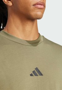 T-shirt verde oliva in tessuto morbido, con il logo nero Adidas sul petto e un classico collo rotondo.