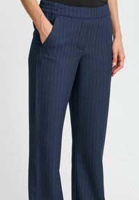 Pantalons bleu marine à rayures avec un tissu lisse, une taille élastique et des poches latérales. La coupe est droite et ajustée, sans embellissements.