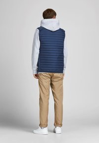Marineblå puffer vest med horisontale syninger, båret over en grå hoodie, parret med beige bukser og hvide sneakers. Enkel design og afslappet pasform.