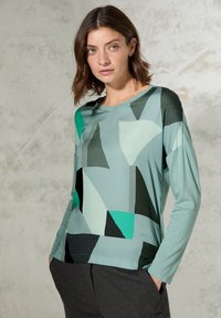 Jasnoniebieska koszula z długim rękawem z abstrakcyjnymi geometrycznymi wzorami w odcieniach teal, czerni i szarości. Gładki materiał o luźnym kroju. Wzór z dekoltem w kształcie litery V.