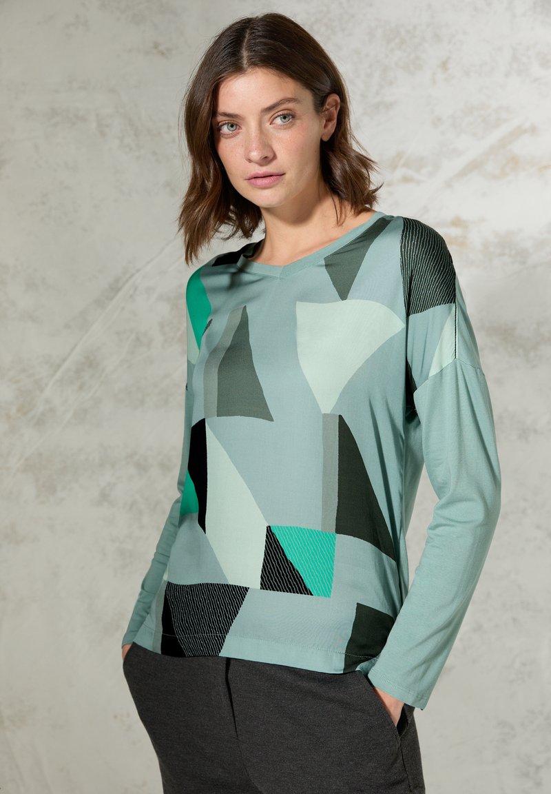 Jasnoniebieska koszula z długim rękawem z abstrakcyjnymi geometrycznymi wzorami w odcieniach teal, czerni i szarości. Gładki materiał o luźnym kroju. Wzór z dekoltem w kształcie litery V.