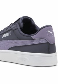 Puma sportbačiai su tamsiai pilku viršumi, violetiniu akcentu, tekstūruota medžiaga, balta tarpine ir PUMA logotipas šone ir ant kulno.