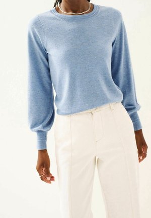 Pull-over en tricot bleu clair avec manches longues légèrement bouffantes et encolure ronde, associé à un pantalon blanc taille haute.