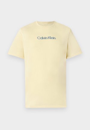 T-shirt en coton jaune clair avec un col rond, des manches courtes et un logo "Calvin Klein" multicolore subtil sur la poitrine.