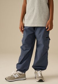 Pantaloni cargo blu navy in materiale leggero con polsini elasticizzati; dotati di tasche laterali e di un accento nero sulla gamba destra. Abbinati a scarpe da ginnastica grigie.