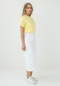 T-shirt in cotone giallo abbinato a pantaloni bianchi a vita alta e a gamba larga, con sneakers bianche, caratterizzato da una vestibilità rilassata e orlo risvoltato.