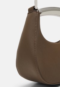 Brązowa skórzana torebka o zakrzywionym kształcie, widoczne szwy i srebrny uchwyt akcentujący. Gładka tekstura z minimalistycznym designem.