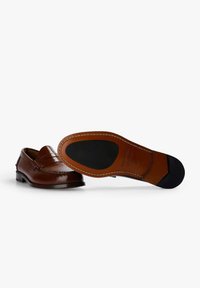 Mocasines de cuero marrón con un detalle de costura, parte superior lisa, un tacón bajo, suela de cuero y un inserto de goma negra en la suela para mayor tracción.
