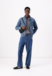 Denim jacket with star pattern, gray t-shirt, loose blue jeans, and black sneakers featuring white accents, completed with a small black bag.