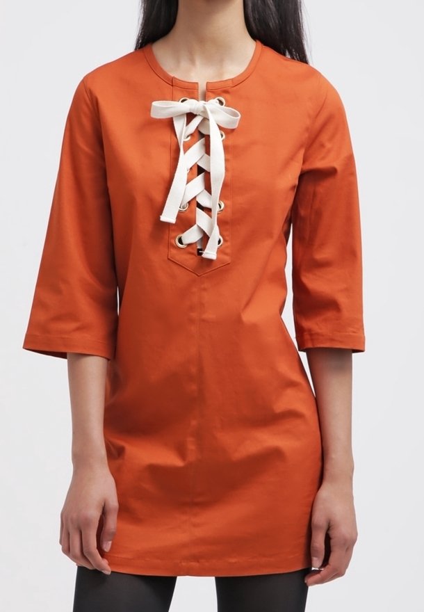 Tunique en coton orange avec un col rond, des manches trois-quarts et un détail de laçage à l'avant avec des liens blancs et des œillets en métal.