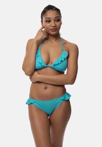 Tirkīza bikini komplekts ar trīsstūrveida topu un vilinošām maliņām, kā arī saskaņotām biksēm ar vilinošām detaļām. Gluda auduma tekstūra.