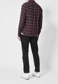 Overhemd met lange mouwen in ruitpatroon, marineblauw en rood, gecombineerd met donkere spijkerbroek en witte hoge sneakers. Voorzien van een standaardkraag en knoopsluiting.