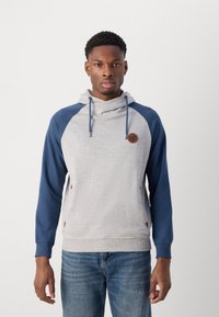 Sudadera con capucha en gris y azul marino, con mangas raglán, cuello con cordón y parche de logo de cuero. Presenta una textura suave y un ajuste relajado.