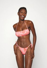 Biquíni rosa com padrão e top bandeau, cuecas com laço lateral, apresentando motivos tropicais. Feito de tecido suave, design ajustado.